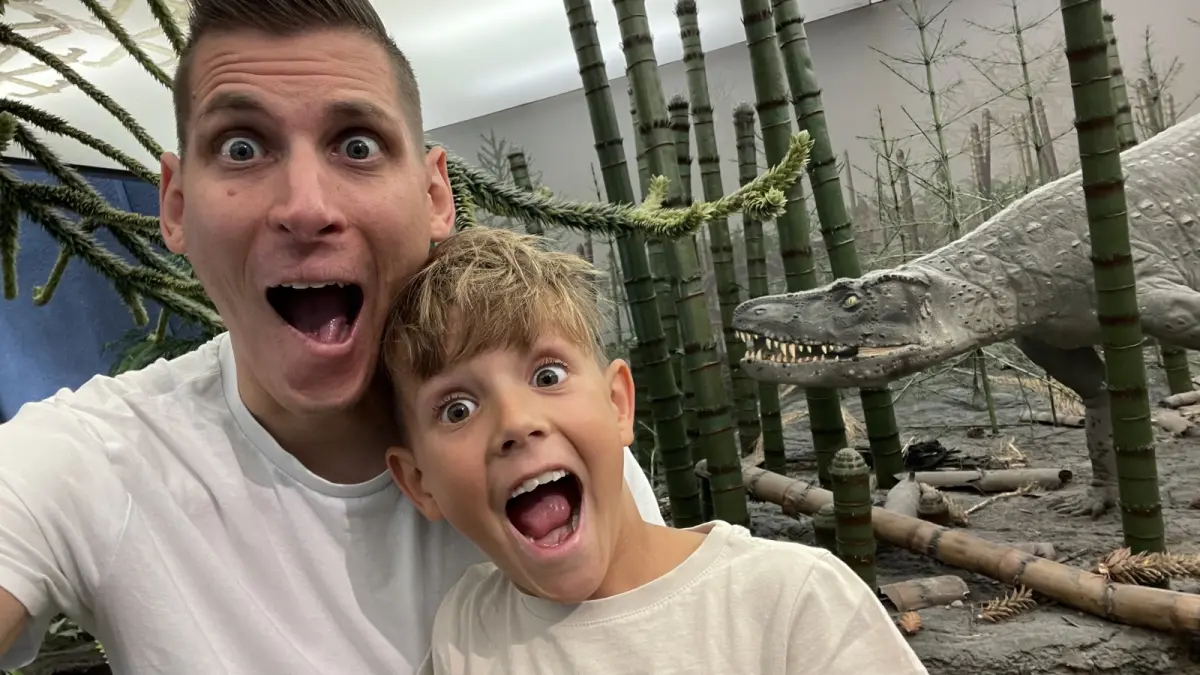Christian Kögler und ein Kind machen im Museum ein lustiges Selfie vor einem Dinosaurier